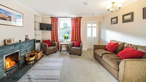 Een woonkamer met een open haard, twee fauteuils, een bank, een televisie en een raam met gordijnen.