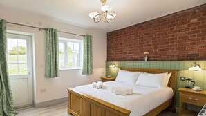 A bedroom with a wooden bed, green curtains, a brick wall, and a window. - 1 bedroom accommodation in Ledbury (Ledbury)