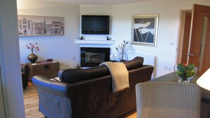 A modern living room with a sofa, a flat-screen TV mounted above a fireplace, and a framed picture on the wall.