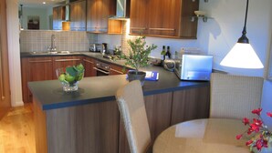A modern kitchen with wooden cabinets, a built-in oven, and a dining area with a table and chairs.