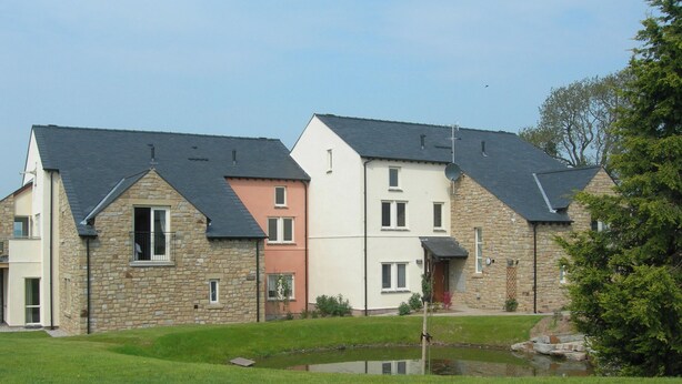 A row of multi-story houses with stone and painted exteriors, a small pond, and a grassy area.