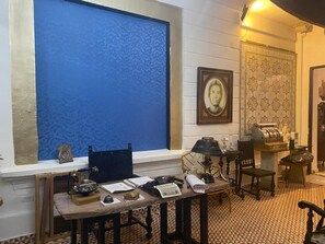 A room with a large blue patterned window, a desk with various items, a framed portrait, and a patterned wall. - Hotel Galería Casa de La Luz   (Bogotá)
