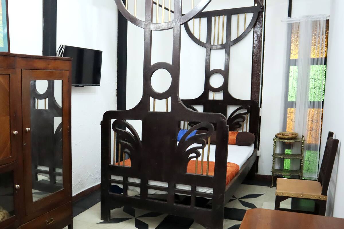A bedroom with a bed, a wooden cabinet, a television, and a window with curtains.