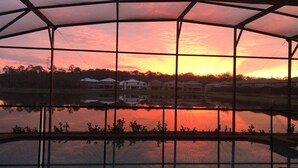 Blick durch ein metallumrandetes Fenster bei Sonnenuntergang, der eine Reihe Häuser gegenüber einer ruhigen Wasserfläche reflektiert.