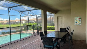 Eine überdachte Terrasse mit Blick auf einen Pool, einem Tisch mit Stühlen und einer Tür.