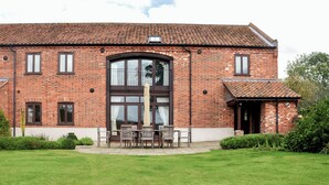 A brick building with a large arched window and a small balcony with outdoor seating. - This charming barn conversion is ideal for a large family holiday. (Sculthorpe, Fakenham)