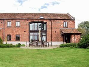 A brick building with a large arched window and a small balcony with outdoor seating.