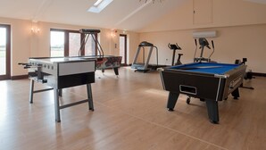 A spacious indoor area with a pool table, a foosball table, exercise equipment, and large windows allowing natural light. - This charming barn conversion is ideal for a large family holiday. (Sculthorpe, Fakenham)
