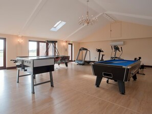 A spacious indoor area with a pool table, a foosball table, exercise equipment, and large windows allowing natural light.