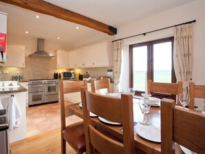 A modern kitchen with stainless steel appliances, wooden chairs, and a dining table set for two.