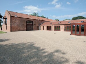 A spacious building with a gravel driveway and a large open area in front. - This charming barn conversion is ideal for a large family holiday. (Sculthorpe, Fakenham)