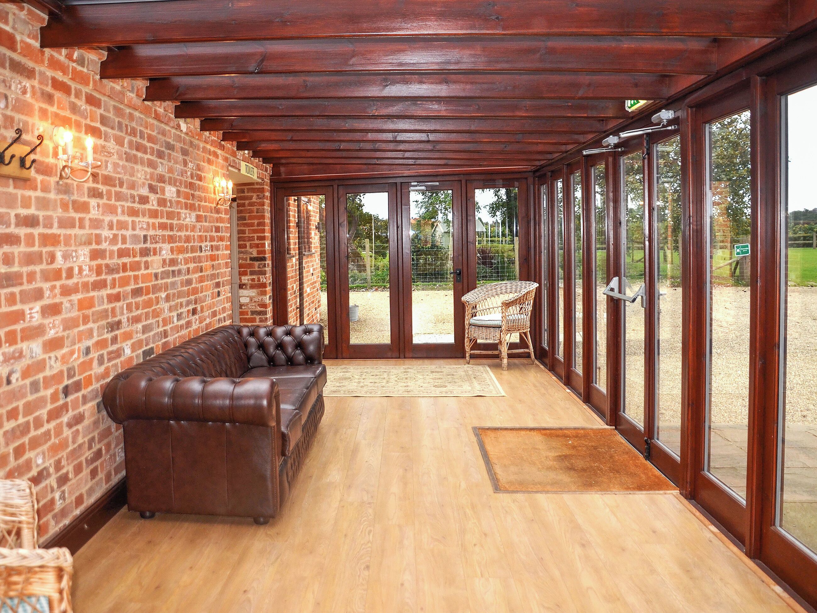 A room with a brick wall, wooden ceiling, a leather sofa, wicker chair, and large windows.