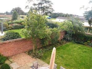 A garden with a brick wall, a grassy lawn, and a variety of plants and trees.