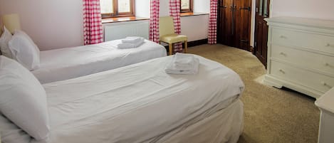 Una camera d'albergo con due letti, una sedia, una cassettiera e una finestra con tende.