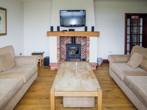 A living room with two sofas, a wooden coffee table, a fireplace, a television mounted above the fireplace, and a door with a window.
