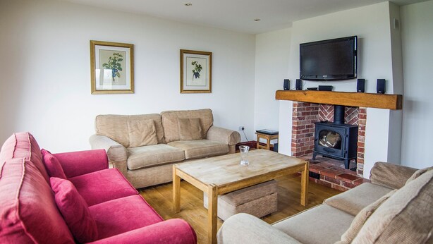 A living room with a fireplace, two sofas, a coffee table, and framed pictures on the wall. - This charming barn conversion is ideal for a large family holiday. (Sculthorpe, Fakenham)