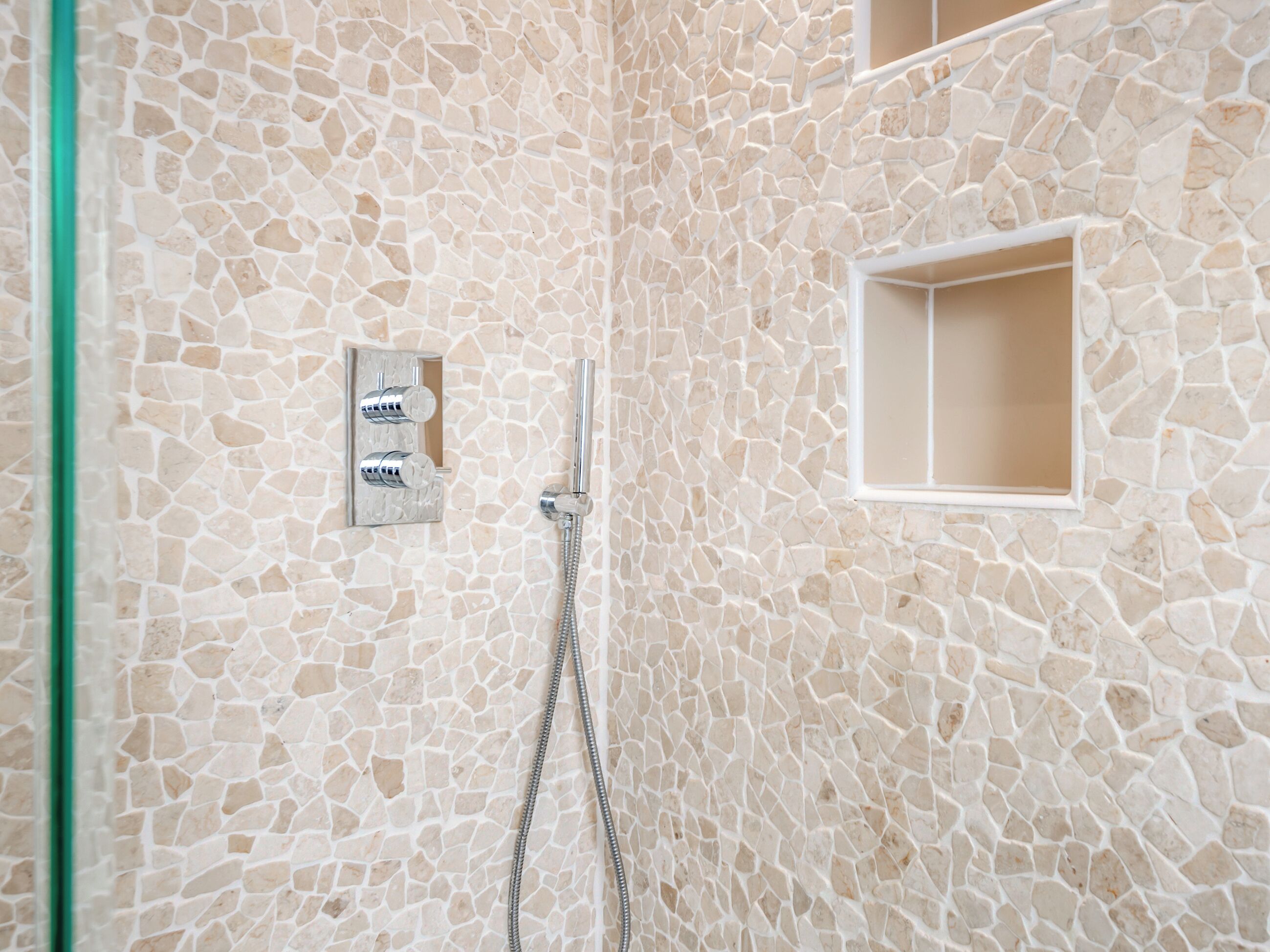 A bathroom with a mosaic wall, a shower, and a small window.