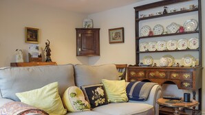 A living room with a sofa, a wooden cabinet with decorative plates, and a small round table. - A delightful cottage offering comfortable accommodation for up to four guests. (Much Birch, near Hereford)