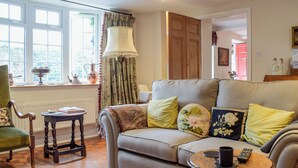 A cozy living room with a sofa, a small table with a remote control, and a lamp. - A delightful cottage offering comfortable accommodation for up to four guests. (Much Birch, near Hereford)