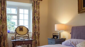 A bedroom with a bed, a bedside table with a lamp, a dresser, a mirror, and a window with curtains. - A delightful cottage offering comfortable accommodation for up to four guests. (Much Birch, near Hereford)