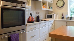 A kitchen with a microwave, kettle, and oven. There are cabinets, a clock, and a window. - A delightful cottage offering comfortable accommodation for up to four guests. (Much Birch, near Hereford)