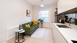 A modern kitchen with a white countertop, a green sofa, and a small dining table with a wine glass. - Trendy Studio on Rose South (Edinburgh)