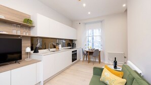 A modern kitchen with white cabinets, a built-in oven, and a dining area with a table and chairs. - Trendy Studio on Rose South (Edinburgh)