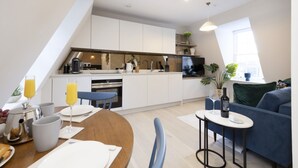 Una cocina moderna con armarios blancos, un comedor con mesa de madera y un sofá azul.