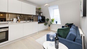 Una cocina moderna con armarios blancos, horno empotrado y una zona de comedor con sofá azul y una mesita redonda.