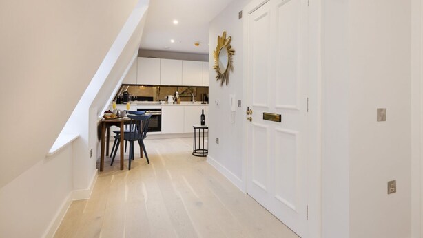 Una cocina moderna con armarios blancos, un comedor con mesa y sillas, y una escalera que sube a un nivel superior.