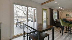 A modern interior with a large sliding glass door leading to an outdoor deck, a wooden dining table with benches, and a bar area with stools.