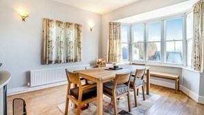 Un comedor con una mesa y sillas de madera, un radiador y una ventana con cortinas.