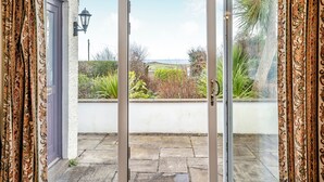Puerta corrediza de vidrio que da a un patio con suelo de piedra y vista al mar.