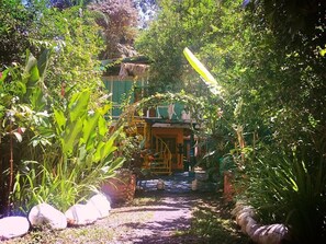 Un sendero de jardín que lleva a un edificio con techo de paja, rodeado de abundante vegetación y plantas en macetas.