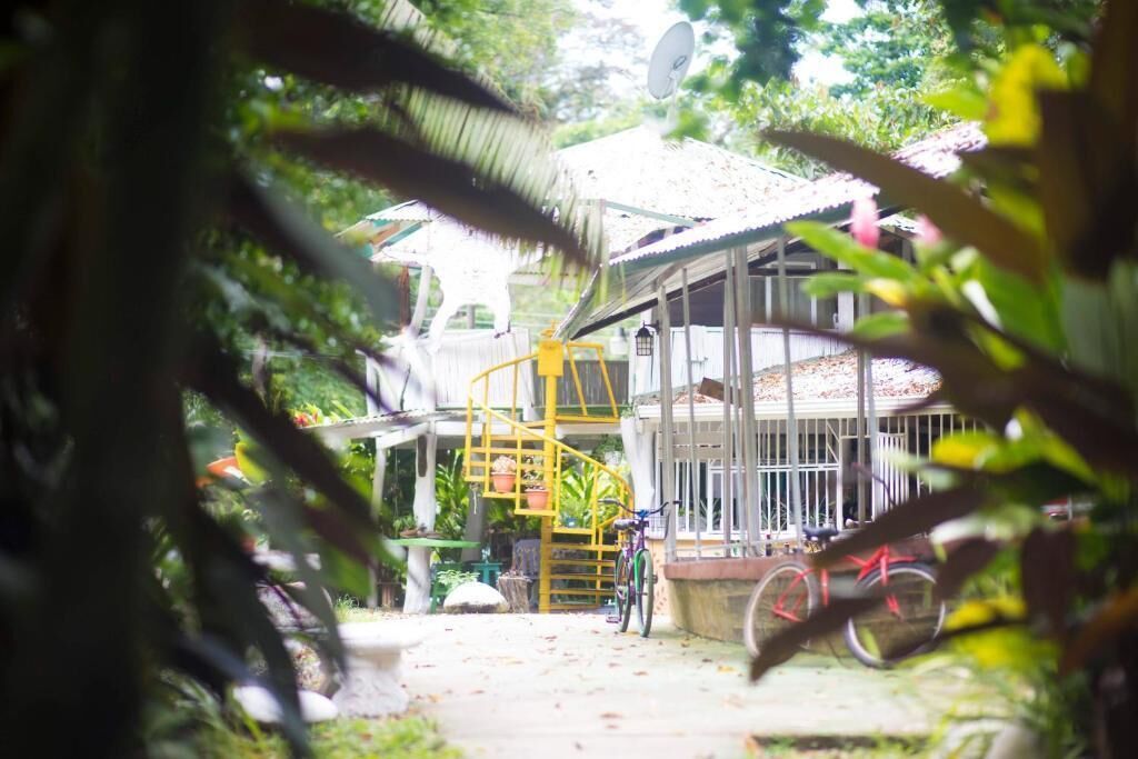 Une maison dotée d’un escalier en colimaçon menant à un balcon, le tout entouré de verdure.