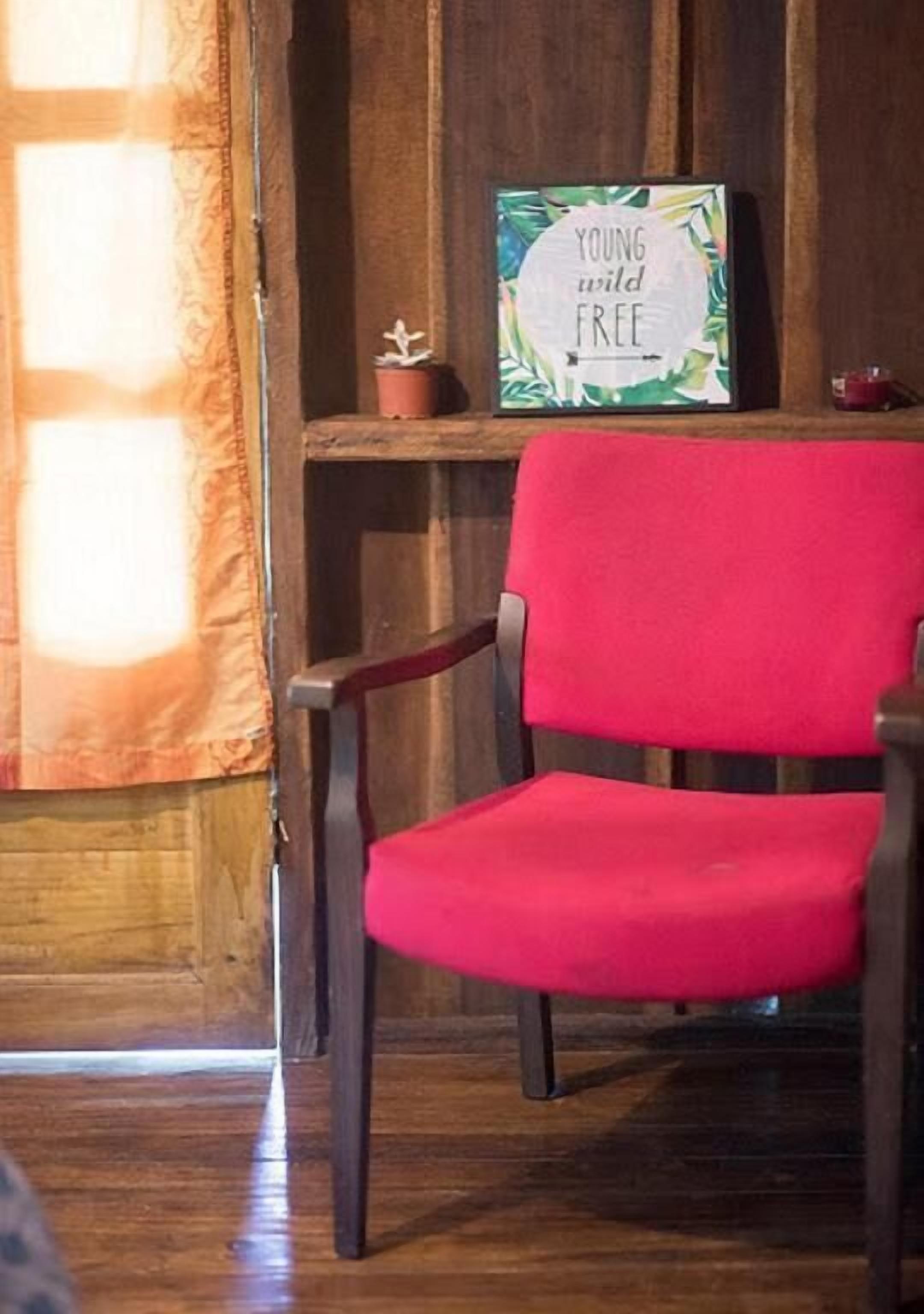 Een rode stoel in een kamer met houten wanden en een raam met gordijnen.