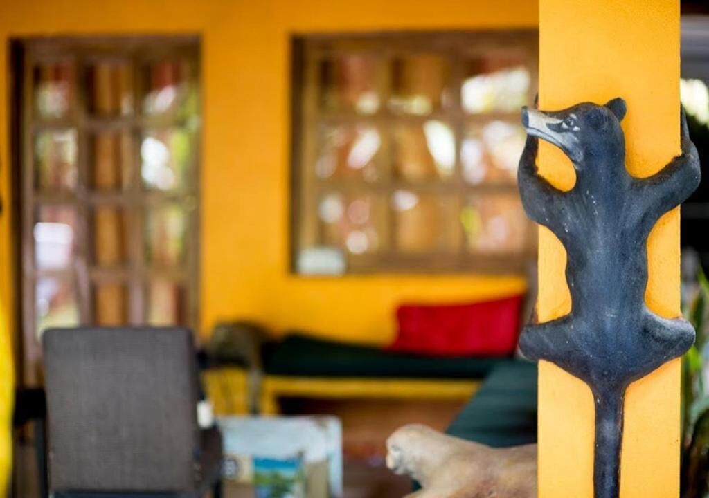 A room with a yellow wall, a black bear sculpture, a window with a view, and a chair.