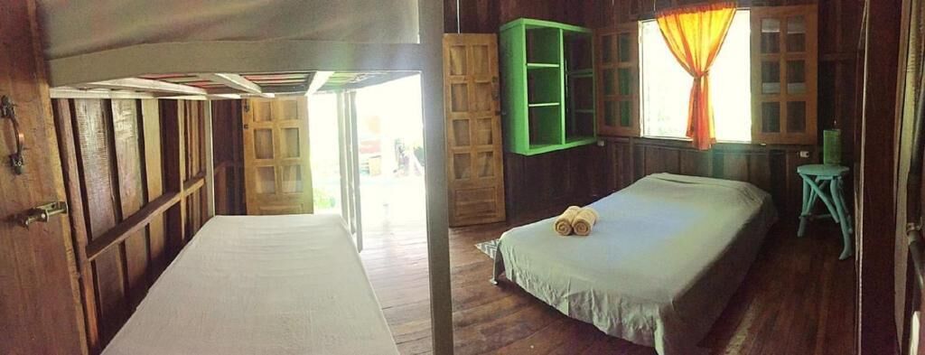 A wooden room with a bed, a green cabinet, and a window with curtains.