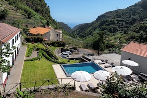 A pool area with lounge chairs and umbrellas, surrounded by a well-maintained lawn and a view of a valley. - Solar dos Reis 2, double room with breakfast (Ribeira Brava)
