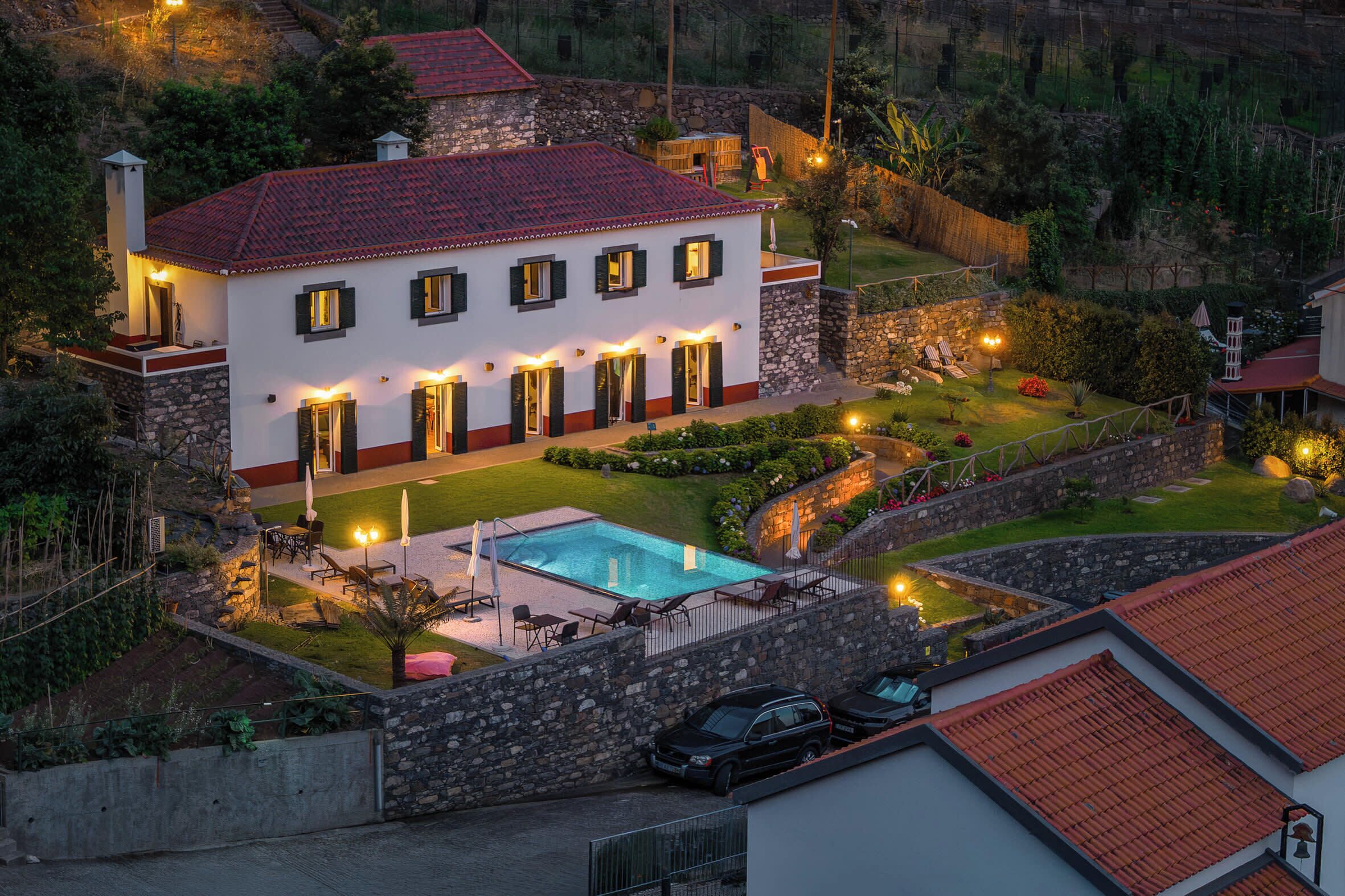 A two-story house with a swimming pool, stone walls, and outdoor lighting.