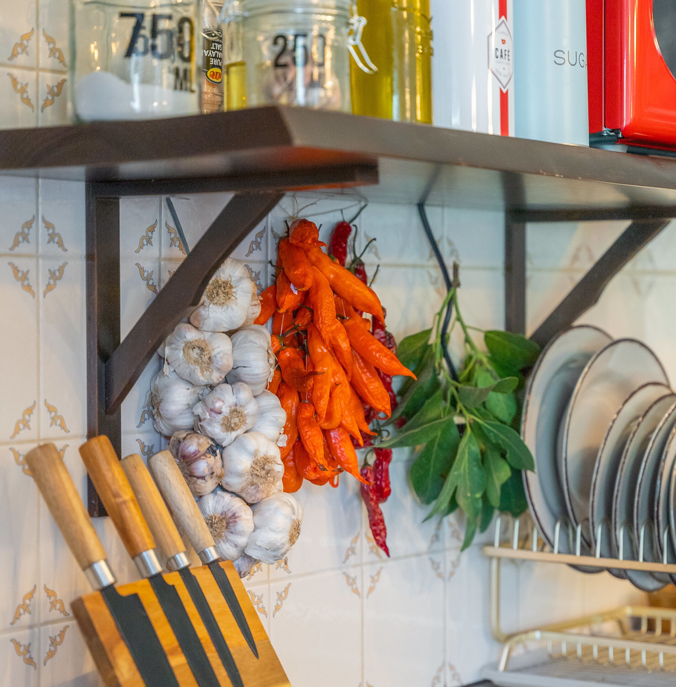 A kitchen counter with garlic, carrots, and a hanging bunch of chili peppers.