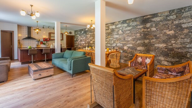 A modern living room with a sofa, wicker chairs, a dining table, and a kitchen in the background.
