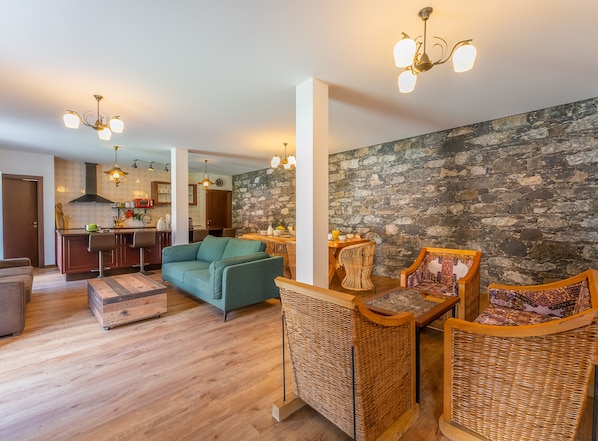 A modern living room with a sofa, wicker chairs, a dining table, and a kitchen in the background.