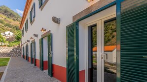 A row of hotel rooms with green shutters, a stone wall, and a cobblestone path.