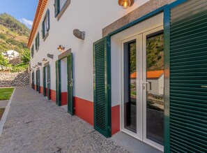 A row of hotel rooms with green shutters, a stone wall, and a cobblestone path.