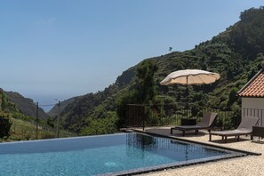 A swimming pool with lounge chairs and an umbrella, surrounded by a mountainous landscape.