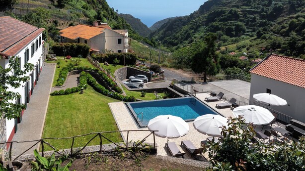 Zona de piscina con sillones de descanso y sombrillas, rodeada por un césped cuidado y vistas a un valle.