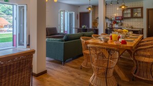 A dining area with wicker chairs, a wooden table set for breakfast, and a view of the outdoors through large windows. - Solar dos Reis 6, double room with breakfast (Ribeira Brava)