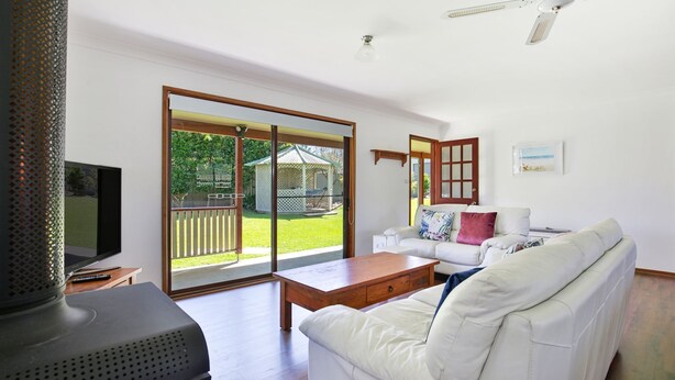 A spacious living room with a white sofa, a wooden coffee table, and a large sliding glass door leading to a backyard. - Callala Calm - Pet Friendly - 5 Mins Walk to Beach (Callala Bay)