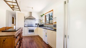 A compact kitchen with white cabinetry, a wooden countertop, a built-in oven, a dishwasher, and a window with a view of trees. - Callala Calm - Pet Friendly - 5 Mins Walk to Beach (Callala Bay)